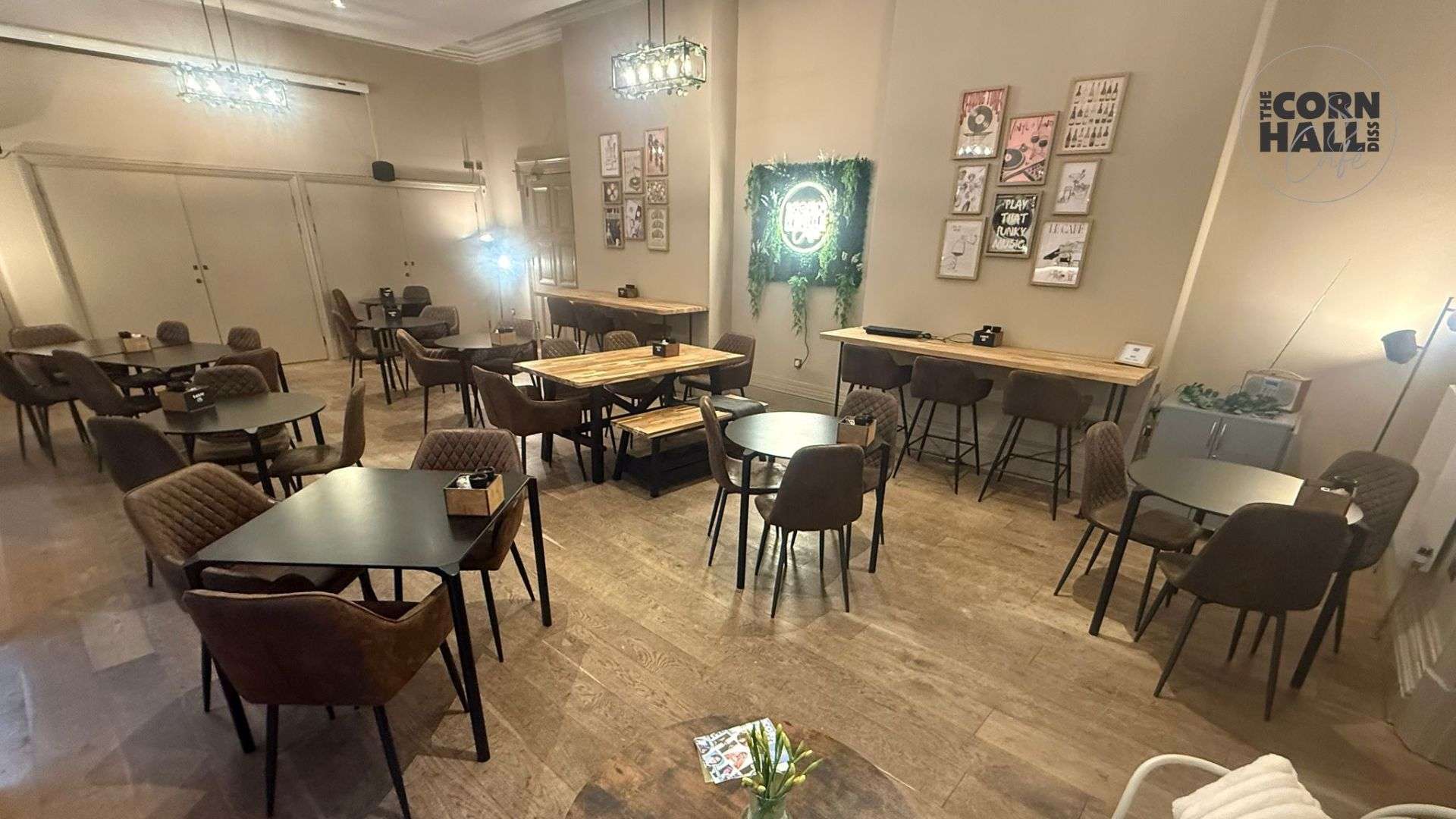 Seating area inside Corn Hall Diss with café tables, chairs and artwork displayed on the walls.