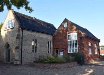 Exterior view of The Pennoyer Centre in Pulham St Mary, showing the restored historic brick and flint buildings under a clear blue sky.