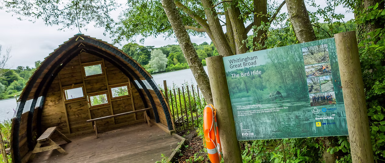 Information board for Whitlingham Great Broad Bird Hide beside the lakeside among mature trees.
