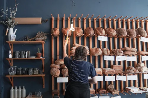 Customer browsing shelves of artisan bread and baked goods inside Bread Source bakery.