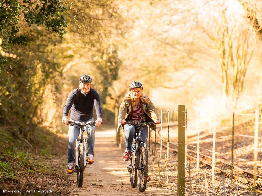 Cyclists enjoying a ride along a tree-lined trail near Aylsham, showcasing the countryside routes available from Bure Valley Cycle Hire.