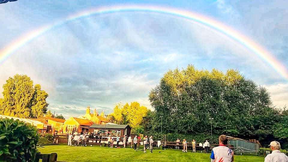 Rainbow arching over the Norfolk countryside near The White Horse pub, with trees, open fields and bright sunshine.