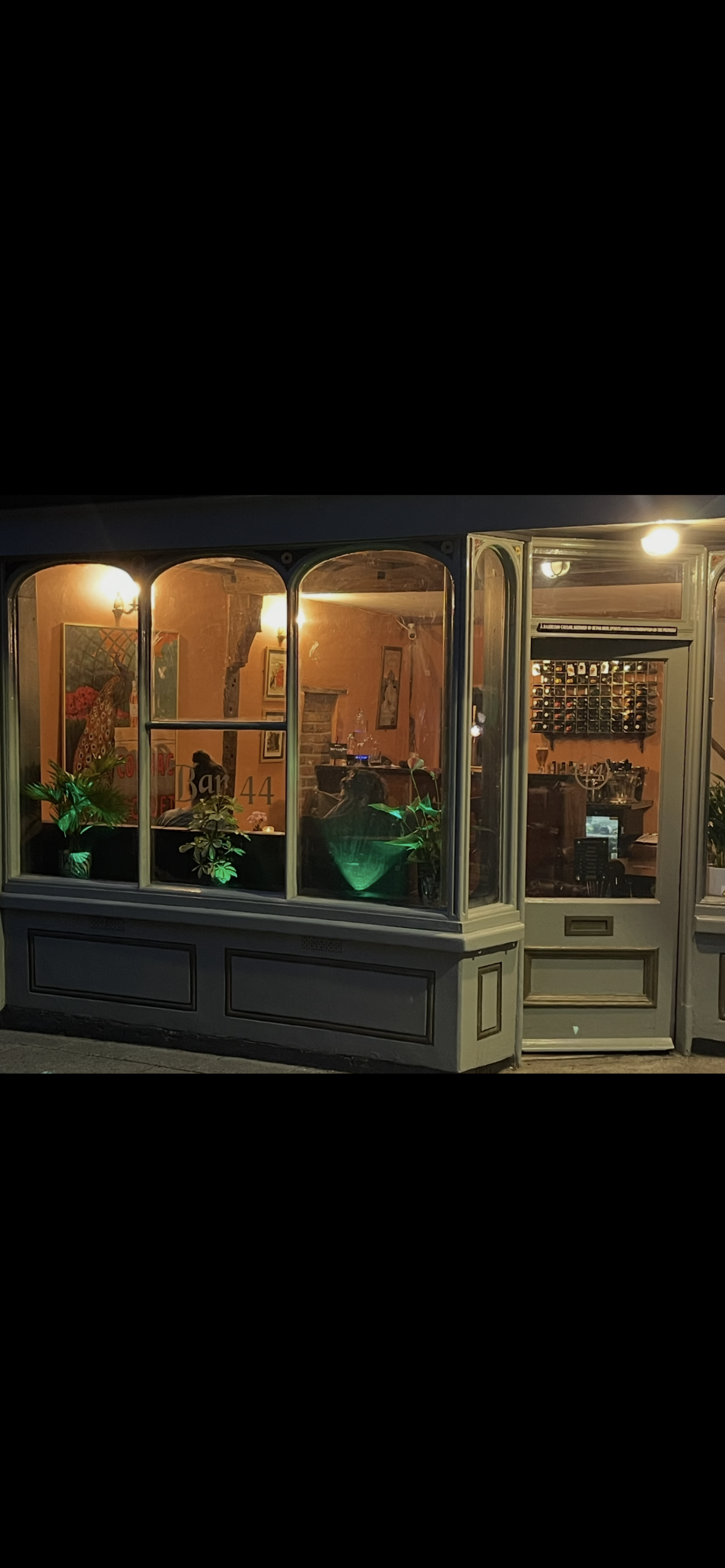 Evening view of Bar 44 in Aylsham, showing the stylish frontage and warmly lit interior through large arched windows.