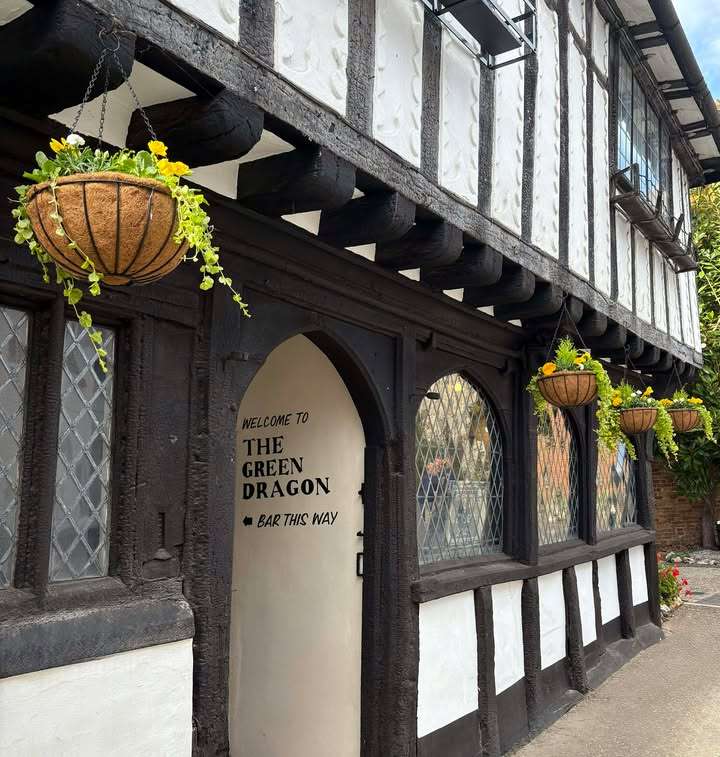 Traditional timber-framed frontage of The Green Dragon in Wymondham, featuring hanging flower baskets, historic black-and-white architecture and the pub entrance.