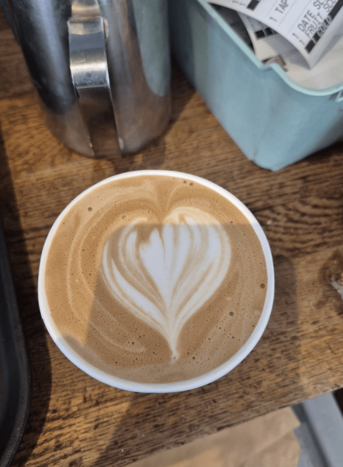 Latte with heart-shaped latte art served on a wooden table at A Piece of Cake café in Coltishall.