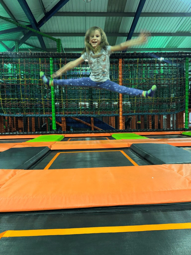 Child jumping on interconnected trampolines at High Altitude indoor adventure centre, with netted play areas and activity zones in the background.