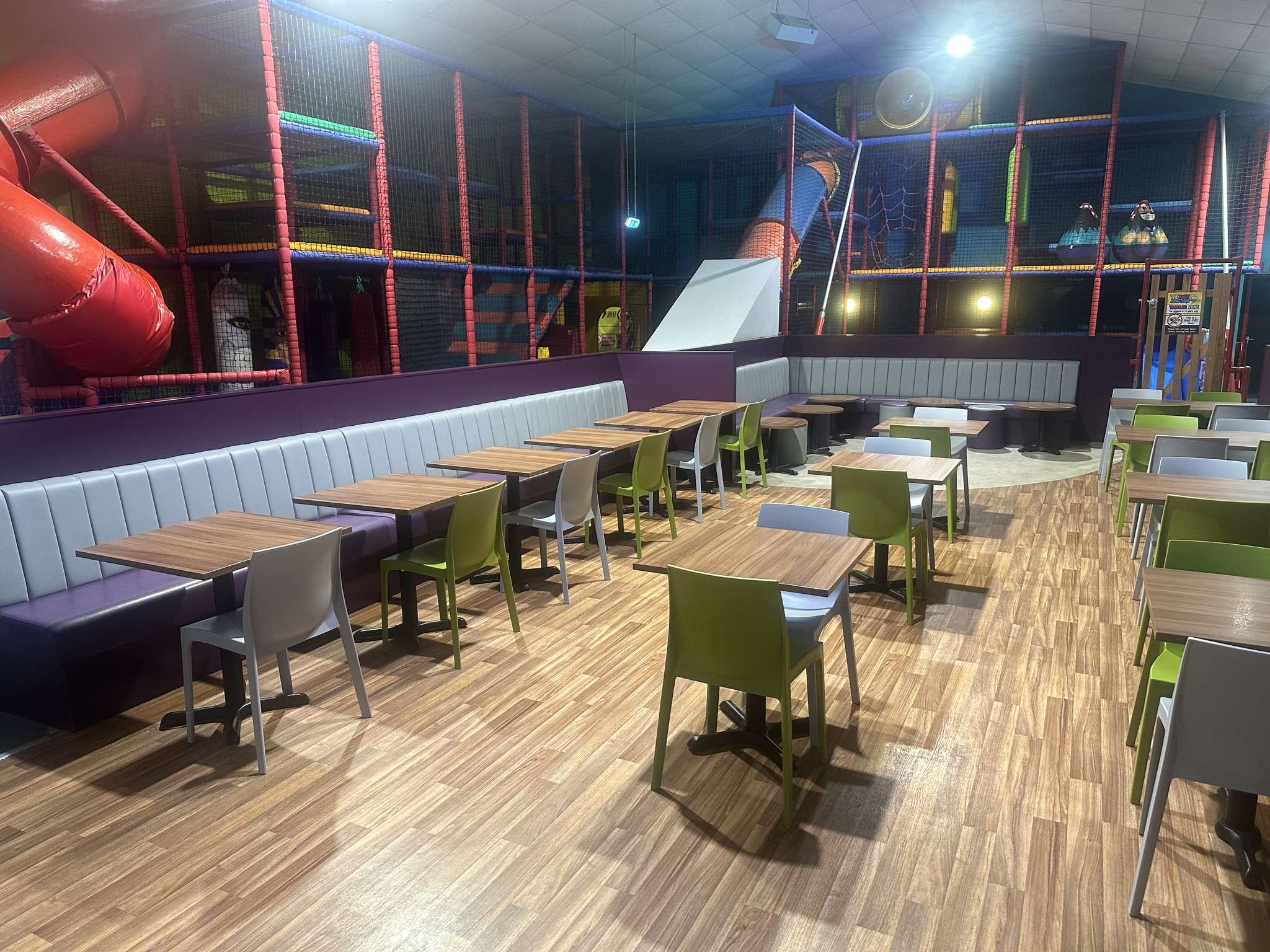 Spacious café seating area overlooking the indoor soft play centre at The Jolly Junction, with tables, chairs and play equipment in the background.